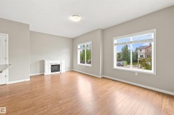 Spacious living area featuring wood-finish flooring, a white electric fireplace, and two large windows with blinds - 
