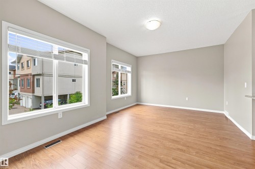 Spacious room featuring wood-finish flooring, light grey painted walls, white baseboards, and two windows with blinds - #144 104 West Haven Dr, Leduc, AB - Indoor Photo Showing Other Room