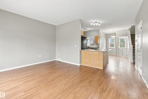 Open-concept living space featuring wood-finish flooring, light gray wall paint, and white baseboards - #144 104 West Haven Dr, Leduc, AB - Indoor