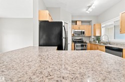 Kitchen featuring light wood cabinetry, granite-style countertops, stainless steel appliances, and a double basin sink with a high-arc faucet - 