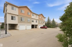 Multi-level townhouse exterior featuring stucco cladding, multiple windows with white frames, individual garage doors, and mature evergreen trees - 