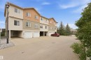 Multi-level townhouse exterior featuring stucco cladding, multiple windows with white frames, individual garage doors, and mature evergreen trees - #144 104 West Haven Dr, Leduc, AB  - Outdoor 