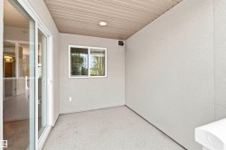 Outdoor patio with textured concrete flooring, white stucco walls, and a white aluminum sliding door - 