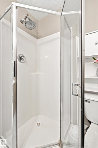 Corner shower enclosure featuring a glass door, chrome hardware, a fixed showerhead, and a white shower base - #144 104 West Haven Dr, Leduc, AB - Indoor Photo Showing Bathroom