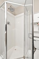 Corner shower enclosure featuring a glass door, chrome hardware, a fixed showerhead, and a white shower base - 
