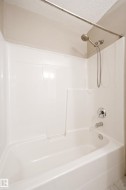 Bathtub and shower combination featuring a white surround, chrome fixtures, and a curved shower rod - 
