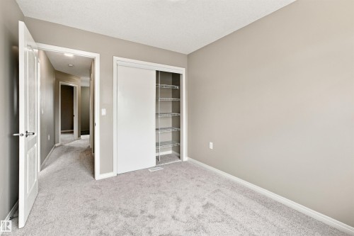 Neutral-toned room featuring light gray carpeting, a built-in closet with sliding doors, and integrated wire shelving - #144 104 West Haven Dr, Leduc, AB - Indoor Photo Showing Other Room