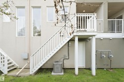 Air Conditioner. Rear exterior featuring an upper-level deck with white railings, direct stair access to the ground level, and a ground-level access door - 