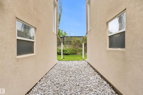 Gravel pathway bordered by stucco-finished walls and leading to a grassy area - #144 104 West Haven Dr, Leduc, AB - Outdoor With Exterior