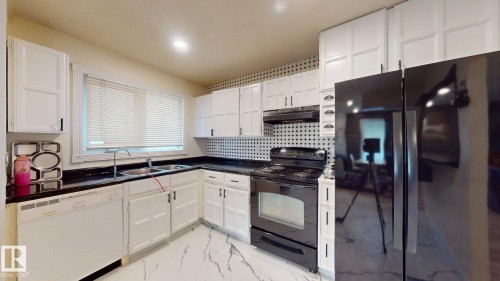 Kitchen featuring white cabinetry, dark countertops, black appliances, a double basin sink, and a patterned backsplash - 12812 45 Street Nw, Edmonton, AB - Indoor Photo Showing Kitchen With Double Sink
