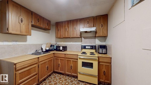 Kitchen featuring abundant wood cabinetry, light wood-finish countertops, and a full-size range with overhead ventilation - 12812 45 Street Nw, Edmonton, AB - Indoor Photo Showing Kitchen