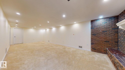 Spacious room featuring neutral carpeting, recessed lighting, and a brick accent wall with a fireplace surround and hearth - 12812 45 Street Nw, Edmonton, AB - Indoor Photo Showing Other Room