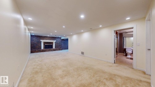 Spacious finished lower level featuring recessed lighting, plush carpeting, and a brick fireplace with a white mantel - 12812 45 Street Nw, Edmonton, AB - Indoor Photo Showing Other Room