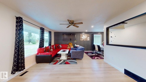 Spacious living area featuring light wood-finish flooring, a contemporary ceiling fan, recessed lighting, and a black brick-pattern accent wall - 12812 45 Street Nw, Edmonton, AB - Indoor