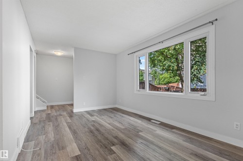 Spacious room with wood-finish flooring, white trim, and a large window - #9 14230 80 St Nw, Edmonton, AB - Indoor Photo Showing Other Room