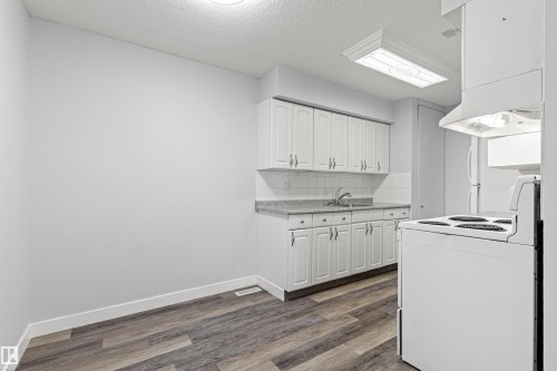 Galley kitchen with wood-finish flooring, white cabinetry, tile backsplash, and a wall-mounted range hood - #9 14230 80 St Nw, Edmonton, AB - Indoor Photo Showing Kitchen