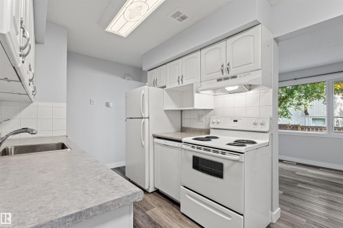 Kitchen featuring white cabinetry, a stainless steel sink, light-toned countertops, white appliances, and wood-finish flooring - #9 14230 80 St Nw, Edmonton, AB - Indoor Photo Showing Kitchen