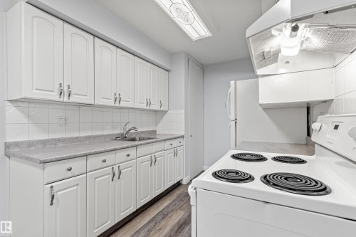 Kitchen featuring white cabinetry, grey countertops, white tile backsplash, and wood-finish flooring - #9 14230 80 St Nw, Edmonton, AB - Indoor Photo Showing Kitchen