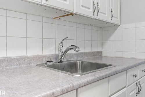 White paneled cabinetry, laminate countertops, stainless steel sink, chrome faucet, and tiled backsplash - #9 14230 80 St Nw, Edmonton, AB - Indoor Photo Showing Kitchen