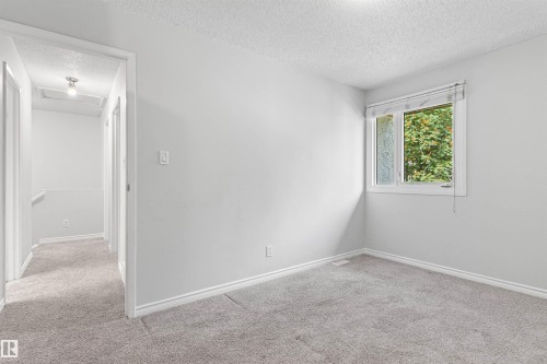 Bright secondary bedroom with neutral wall finishes, plush carpeting, and natural light from a casement window framed by lush exterior greenery - #9 14230 80 St Nw, Edmonton, AB - Indoor Photo Showing Other Room