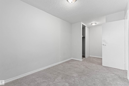 Neutral gray carpeting, white painted walls, white baseboards, and a built-in closet with sliding doors - #9 14230 80 St Nw, Edmonton, AB - Indoor Photo Showing Other Room