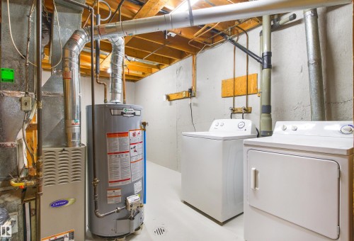Utility room featuring a gas water heater with insulated piping, electric dryer, front-load washing machine, and exposed beam ceiling with yellow-painted wood trusses - #9 14230 80 St Nw, Edmonton, AB - Indoor Photo Showing Basement