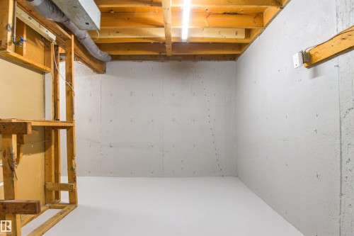 Unfinished basement with exposed wooden joists and concrete walls, featuring an overhead fluorescent light fixture - #9 14230 80 St Nw, Edmonton, AB - Indoor