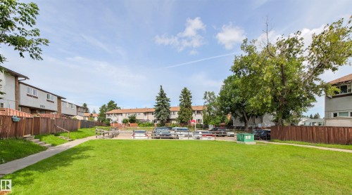 Expansive green space with a paved pathway, surrounded by wood fencing and mature trees - #9 14230 80 St Nw, Edmonton, AB - Outdoor