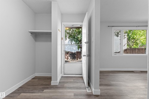 Wood-finish flooring, white walls, built-in closet shelving and rod, white trim, and a prominent window - #9 14230 80 St Nw, Edmonton, AB - Indoor Photo Showing Other Room