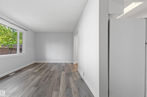 Bright, light-filled room featuring pristine white walls, recessed ceiling lighting, and engineered wood-finish flooring in a warm gray tone - #9 14230 80 St Nw, Edmonton, AB - Indoor Photo Showing Other Room