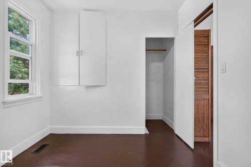 Rich wood-finish flooring with white baseboards, a double-hung window, and built-in wall cabinetry - 9921 109 Street, Fort Saskatchewan, AB - Indoor Photo Showing Other Room