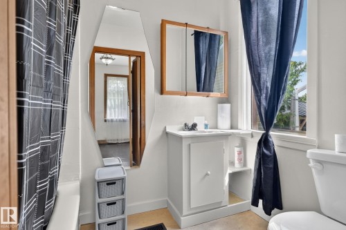 Bright, light-filled bathroom featuring a pedestal sink with chrome faucet, wood-frame mirror, wood-finish flooring, and white subway tile walls - 9921 109 Street, Fort Saskatchewan, AB - Indoor