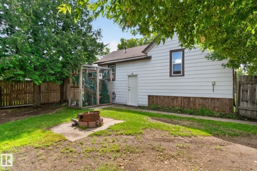 Fenced backyard with mature trees, a built-in fire pit on a concrete pad, and a white siding exterior - 9921 109 Street, Fort Saskatchewan, AB - Outdoor