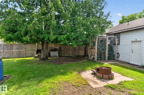 Expansive backyard featuring a manicured lawn, established trees, wood fencing, and a built-in fire pit on a concrete pad - 9921 109 Street, Fort Saskatchewan, AB - Outdoor