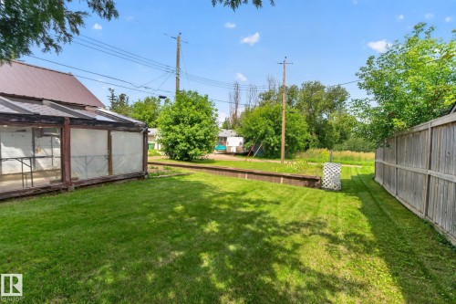 Expansive green lawn with a wood-framed greenhouse structure, wood privacy fencing, and a raised planter bed - 9921 109 Street, Fort Saskatchewan, AB - Outdoor