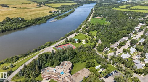 Aerial view showcasing a contemporary residence with manicured grounds and mature landscaping situated along a tranquil riverfront setting - 9921 109 Street, Fort Saskatchewan, AB - Outdoor With Body Of Water With View