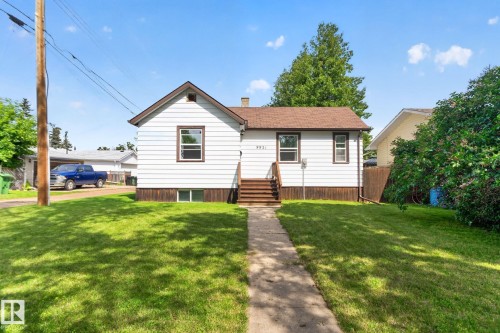 White siding exterior with a brown shingle roof, wood-tone trim, and a concrete pathway leading to a front porch with wood stairs - 9921 109 Street, Fort Saskatchewan, AB - Outdoor