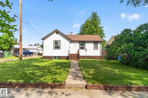 Classic single-story home featuring white horizontal siding, a pitched roof with brick chimney, and front entry stairs - 9921 109 Street, Fort Saskatchewan, AB - Outdoor