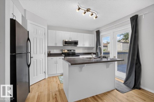 Kitchen featuring white cabinetry, dark countertops, stainless steel appliances, a center island with sink, and wood-finish flooring - 722 88A Street Sw, Edmonton, AB - Indoor Photo Showing Kitchen