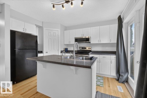 White cabinetry with dark countertops, stainless steel appliances, wood-finish flooring, track lighting, and a kitchen island with an integrated sink - 722 88A Street Sw, Edmonton, AB - Indoor Photo Showing Kitchen With Double Sink