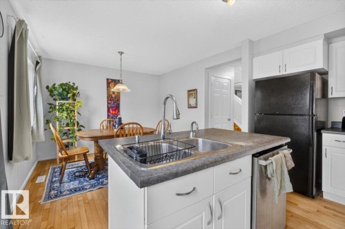 Modern kitchen featuring a large center island with gray composite countertops, stainless steel appliances including a black refrigerator, white cabinetry with hardware accents, and hardwood flooring throughout - 722 88A Street Sw, Edmonton, AB - Indoor Photo Showing Kitchen With Double Sink