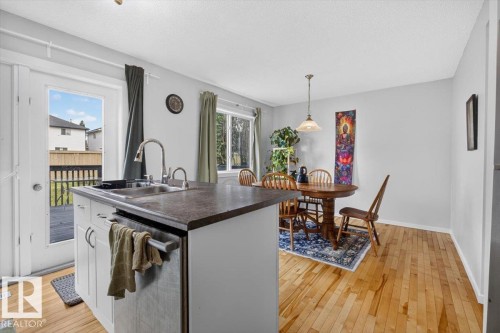 Open-concept kitchen and dining area featuring a large island with a dark wood-finish countertop, white cabinetry, and stainless steel appliances - 722 88A Street Sw, Edmonton, AB - Indoor