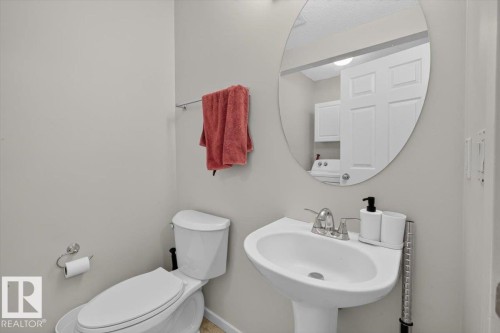 Clean and functional half bath featuring a pedestal sink with chrome faucet, white porcelain toilet, and large circular mirror with integrated lighting - 722 88A Street Sw, Edmonton, AB - Indoor Photo Showing Bathroom