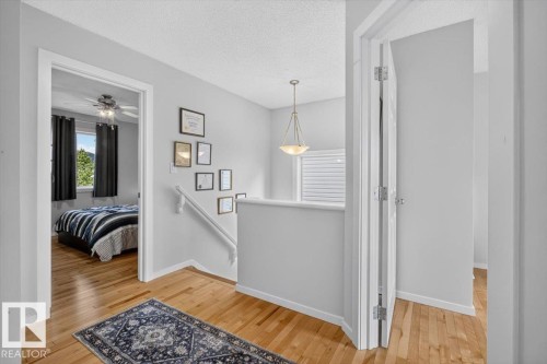Bright hallway showcasing gleaming wood-finish flooring, crisp white trim and walls, pendant lighting fixture, and access to multiple rooms including a primary bedroom suite - 722 88A Street Sw, Edmonton, AB - Indoor Photo Showing Other Room