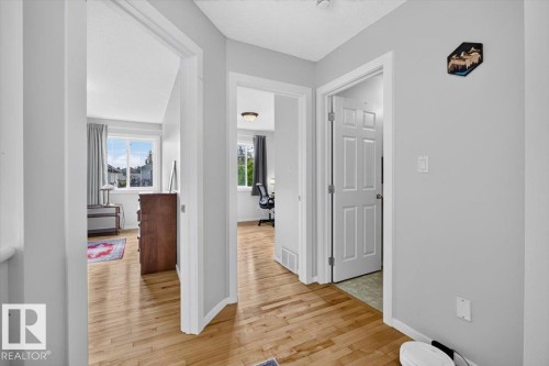 Hardwood-finish flooring throughout the hallway and rooms, white painted walls and trim, and multiple doorways leading to distinct spaces - 722 88A Street Sw, Edmonton, AB - Indoor Photo Showing Other Room