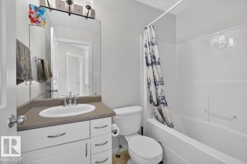 Clean, updated bathroom featuring a white vanity with ample storage, warm wood-finish countertop, oval sink with chrome faucet, white subway tile surround, and a tub-shower combination with coordinating shower enclosure - 722 88A Street Sw, Edmonton, AB - Indoor Photo Showing Bathroom