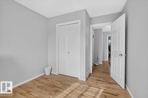 Light-toned wood-finish flooring, white bi-fold closet doors, and white interior doors with satin nickel hardware - 722 88A Street Sw, Edmonton, AB - Indoor Photo Showing Other Room