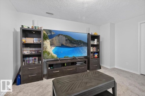 Entertainment-focused recreation room featuring a wall-mounted flat-screen television, built-in dark wood cabinetry with shelving and storage drawers flanking both sides, carpet flooring, and recessed ceiling lighting - 722 88A Street Sw, Edmonton, AB - Indoor Photo Showing Bedroom