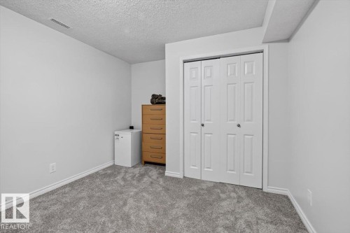 Spacious bedroom with neutral wall finishes, carpeted flooring, double closet doors with panel detailing, and a wooden dresser - 722 88A Street Sw, Edmonton, AB - Indoor