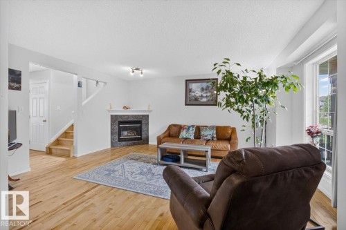 Hardwood flooring throughout, a tiled fireplace with a mantel, and a staircase with wood treads - 722 88A Street Sw, Edmonton, AB - Indoor Photo Showing Living Room With Fireplace
